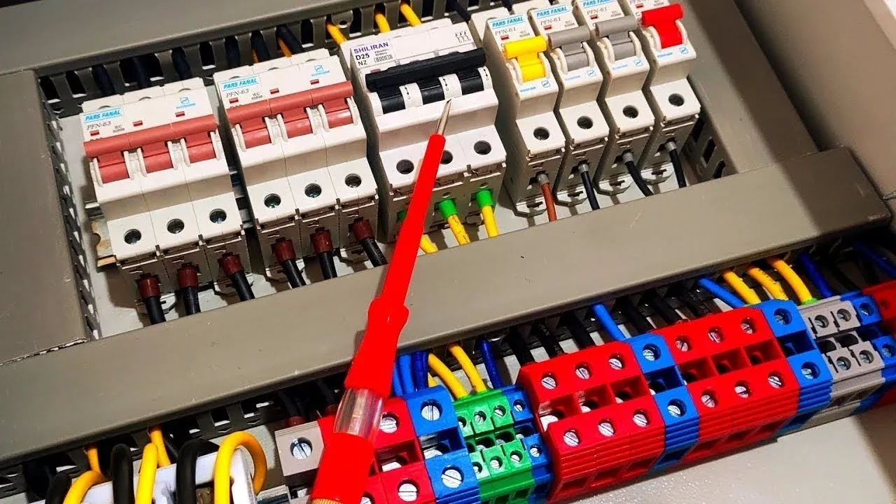 Color coded wires and terminal blocks inside an electrical panel with a voltage tester pen