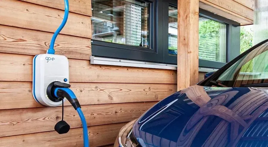 Wall-mounted Level 2 EV charger on a home's exterior wall, plugged into an electric car