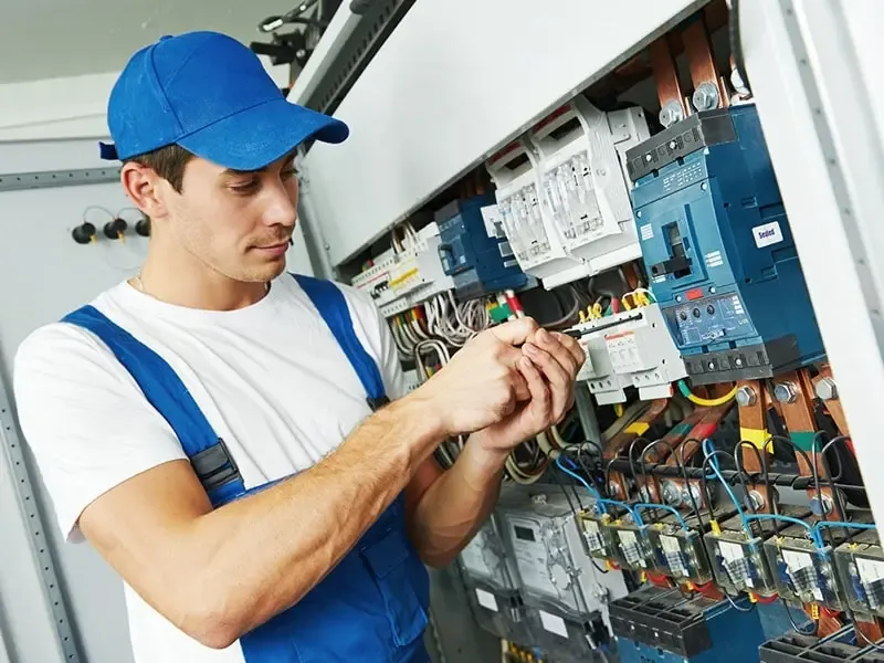 Electrician working on wiring and breakers inside an open electrical distribution panel