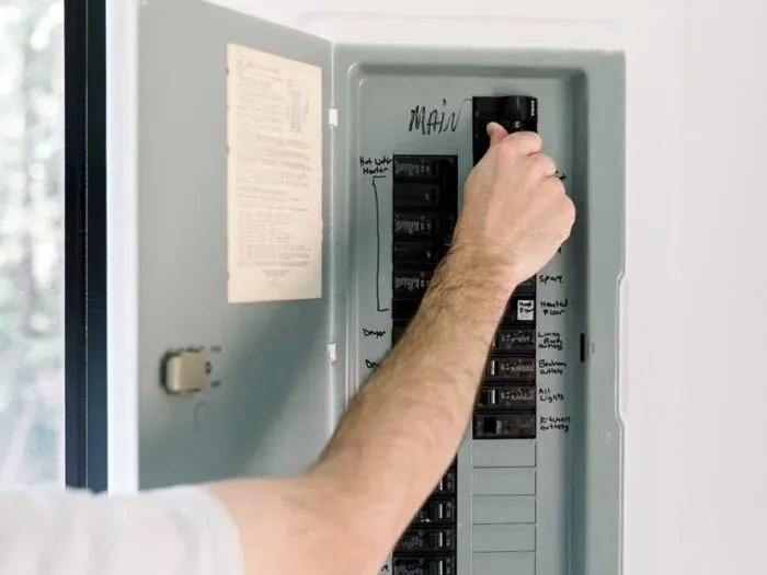 Homeowner reaching for the main breaker in a labeled home electrical panel