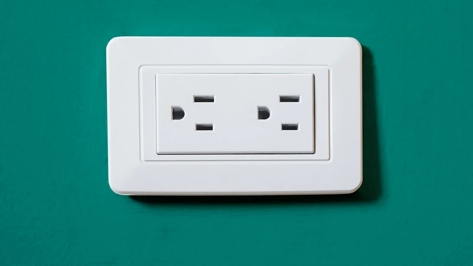 White duplex electrical outlet with a wide cover plate on a green wall