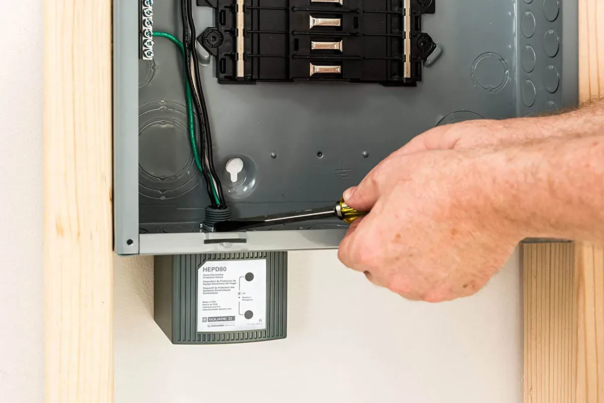 Electrician checking a whole-house surge protector mounted beside a home electrical panel