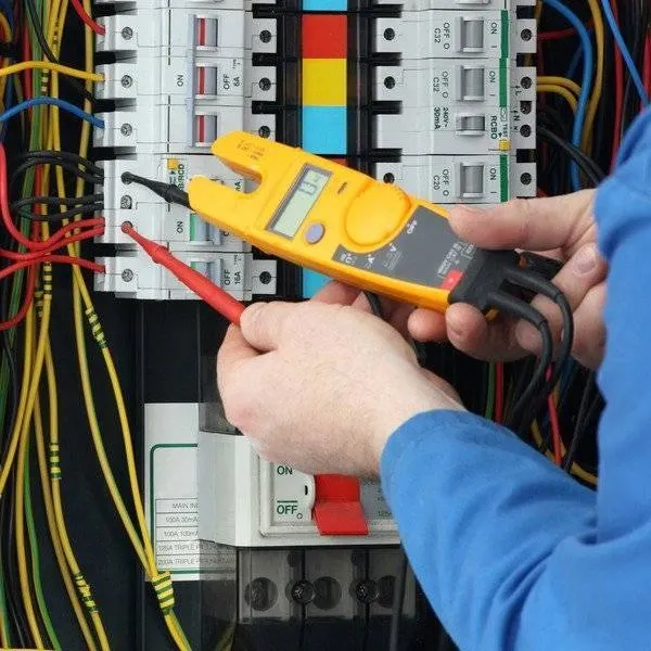 Electrician testing breakers in a commercial electrical panel with a clamp meter