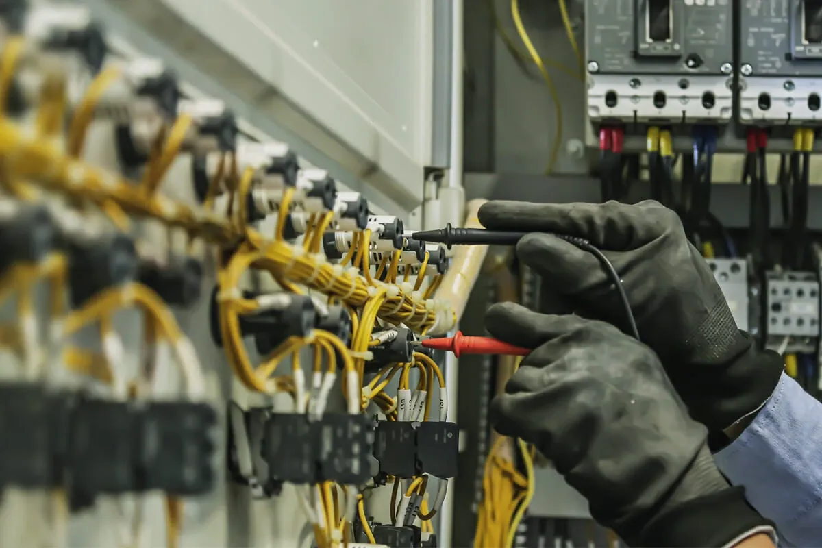 Electrician in work gloves testing control wiring in a commercial electrical cabinet with a meter