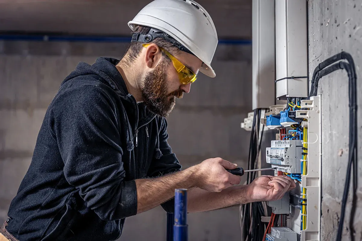 Electrician serving Birchwood Village, MN, in a hard hat and safety glasses wiring breakers in an electrical panel