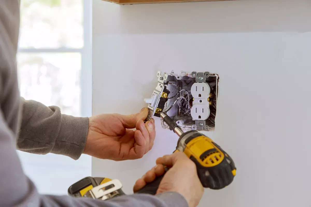 Electrician installing a new outlet and light switch in a wall box