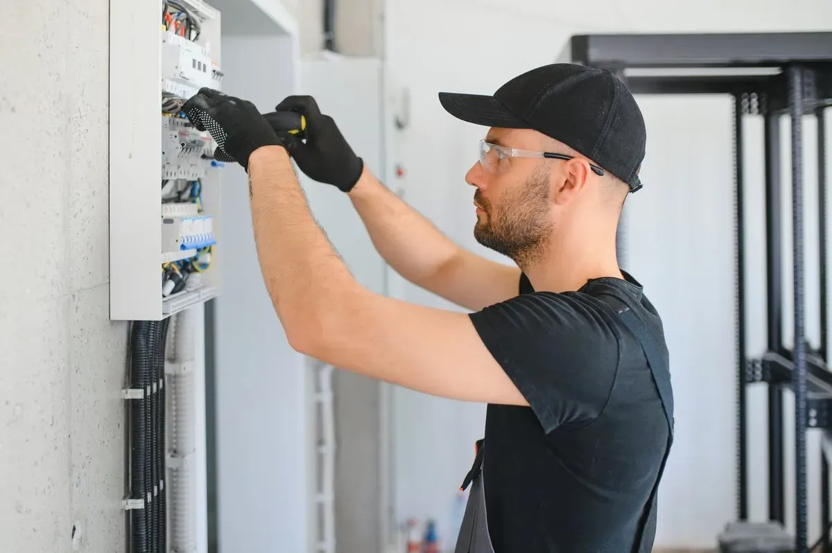 Electrician serving Vadnais Heights, MN, in a cap, safety glasses and gloves working on breakers in an electrical panel