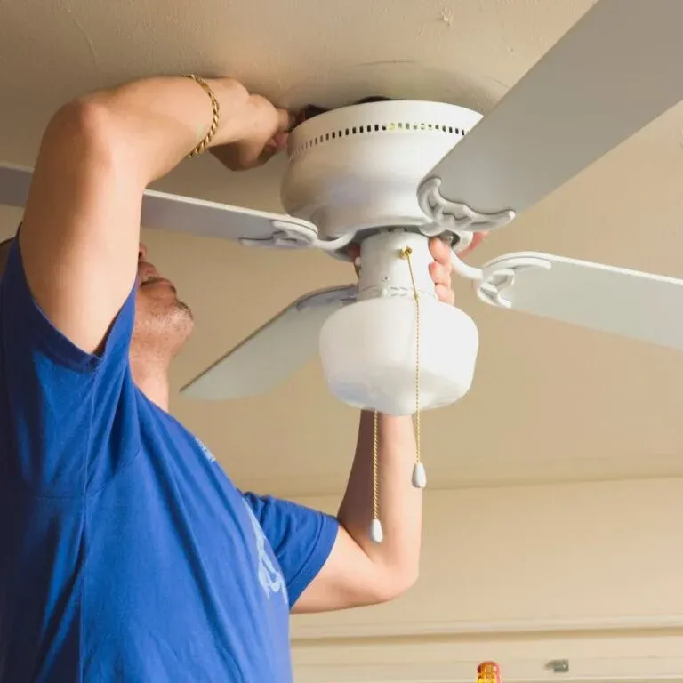 Electrician mounting a white flush mount ceiling fan with a light kit