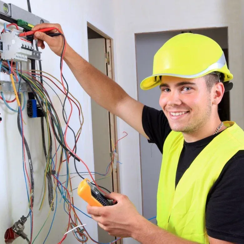 Smiling licensed electrician testing circuit wires at an open electrical panel